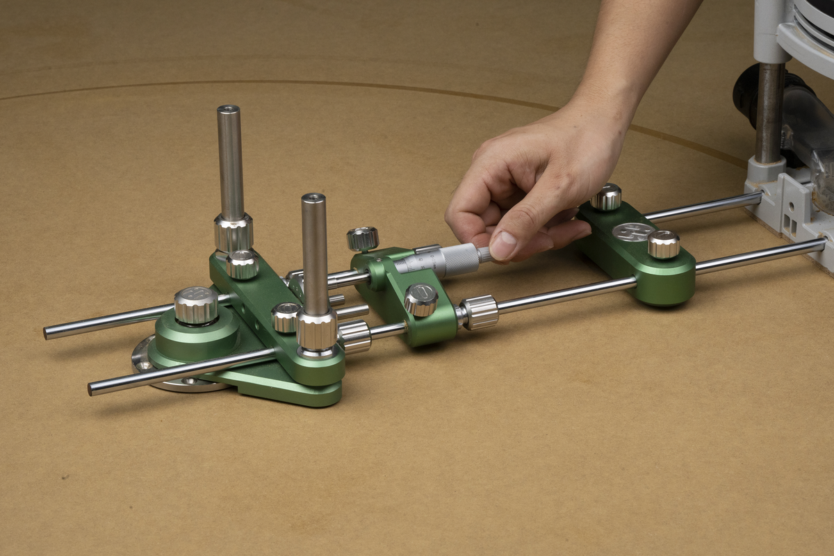 Green router circle-cutting system with guide rails mounted on workbench, hand adjusting
