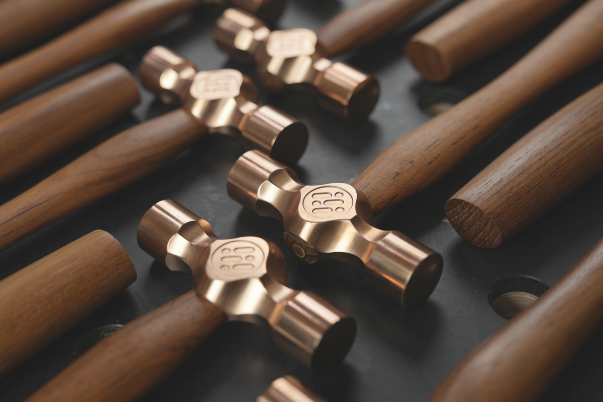 Cross peen hammer set with brass heads and wooden handles on dark surface