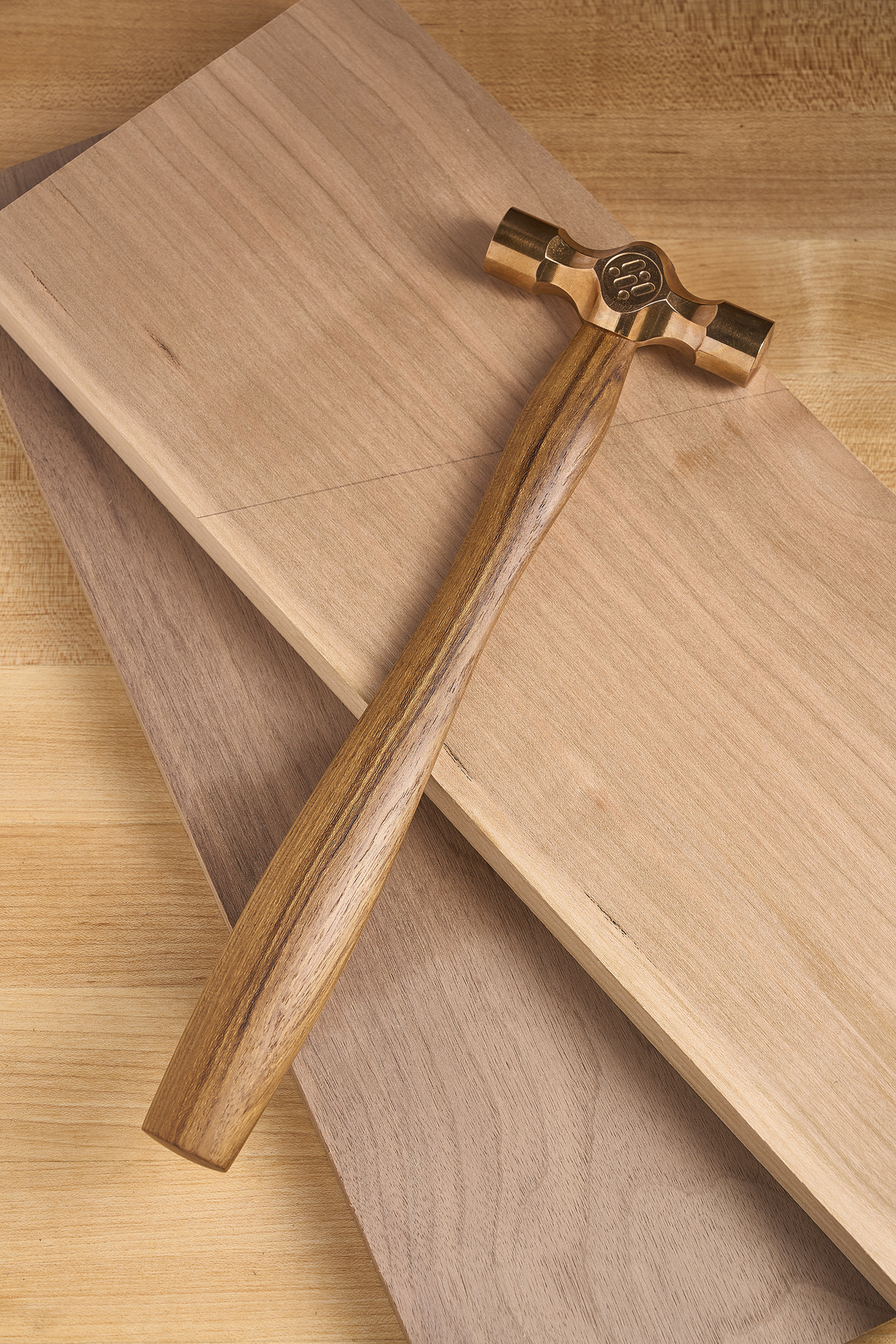 Cross peen hammer with brass head and wooden handle resting on wood boards
